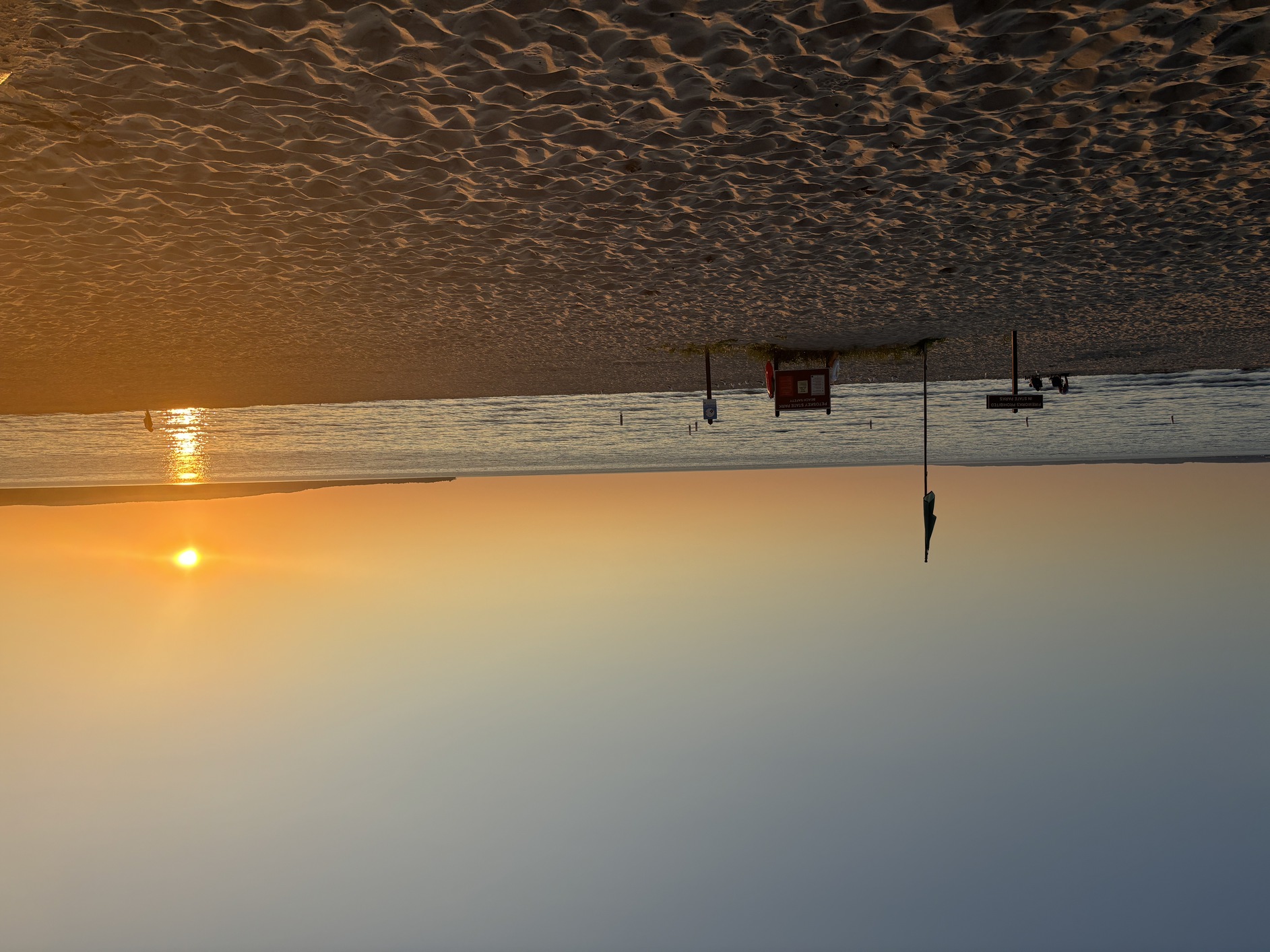 The sun
      is going down over the sand and water at Menonaqua Beach.